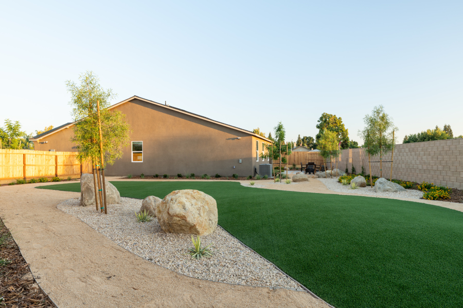 A yard with a large rock in it and a building in the background.