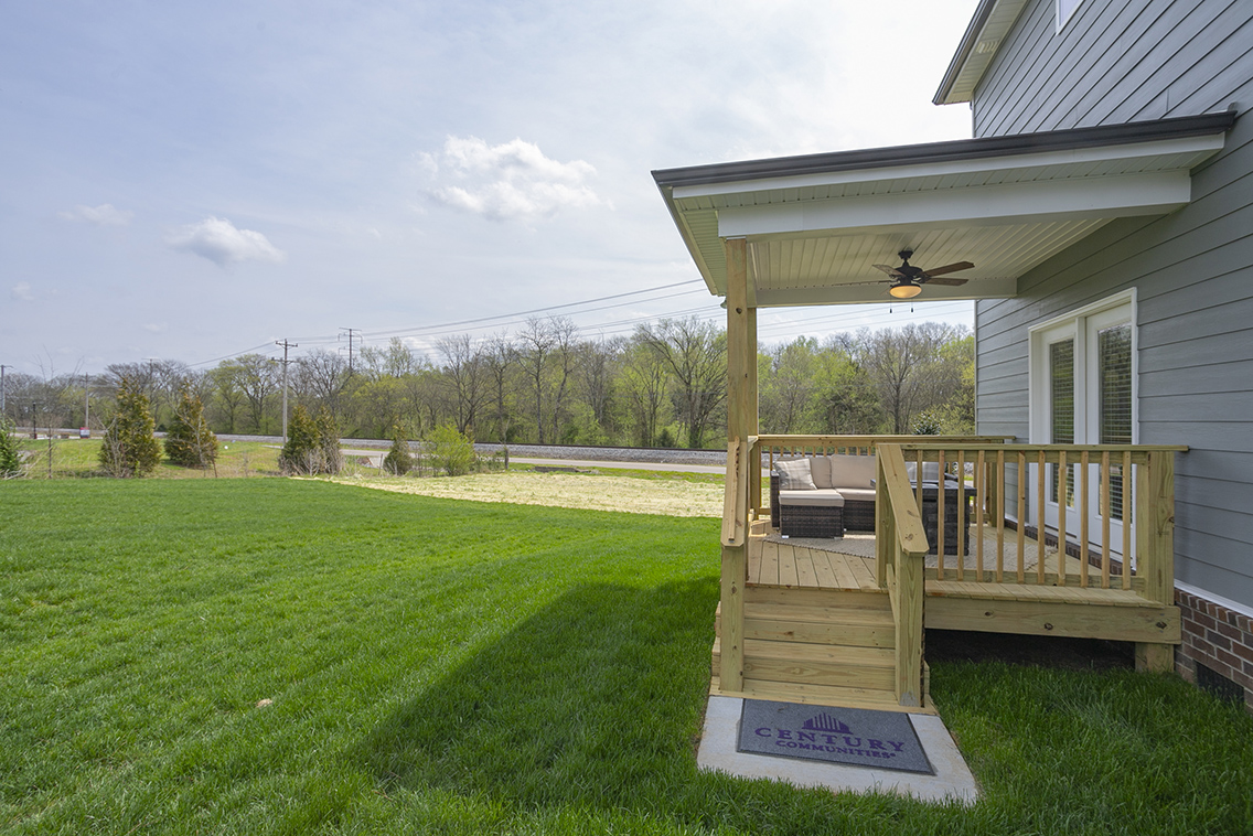 A deck with a railing and a house with a yard and trees in the background.