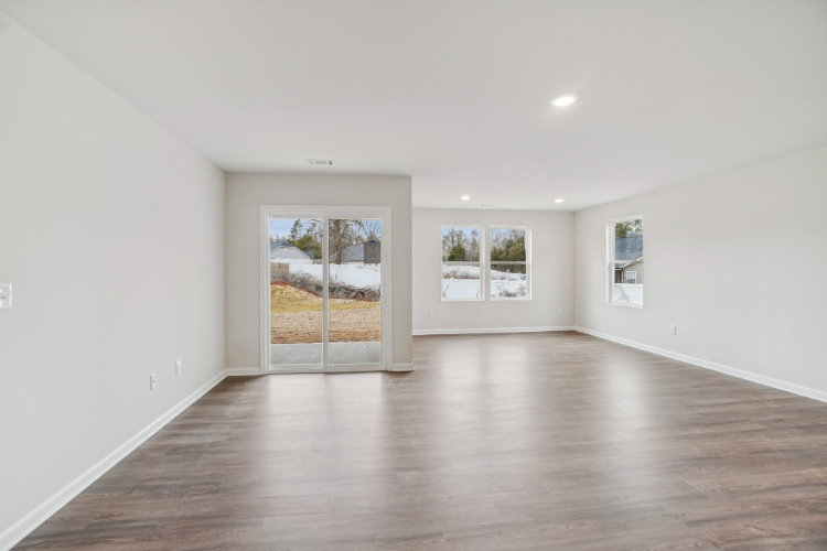 A room with a wood floor and a large window with a view of a bed and a tree.